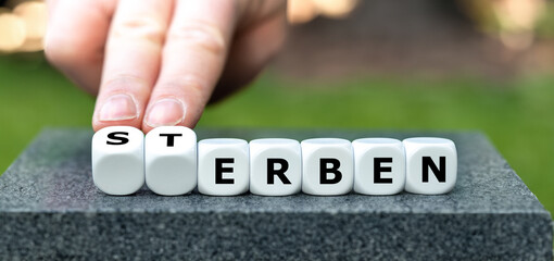 Hand turns dice and changes the German word 'Sterben' (die) to 'erben' (inherit).