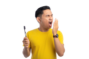 Handsome young Asian man checking his breath with his hand, bad smell from mouth, holding toothbrush isolated on white background