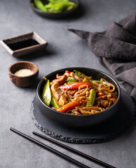Stir-fry with soba noodles, meat and vegetables on dark background with napkin. Asian fast and...