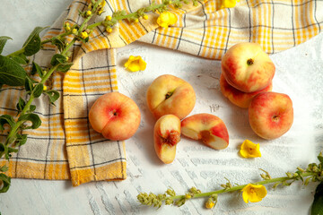 Halves and several whole saturn peaches or flat peach on white wooden background..