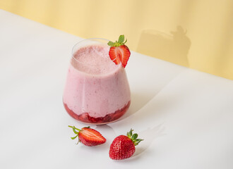 A strawberry milkshake or smoothie in a glass with strawberries on a yellow background
