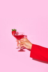 Female hand holding sweet cocktail with strawberry and coconut against pink background. Relaxation. Concept of alcohol and non-alcohol drink, party, holidays, bar, mix. Poster. Copy space for ad