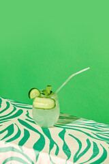 Glass with refreshing sweet and sour cocktail with lien and cucumber taste against green background. Concept of alcohol and non-alcohol drink, party, holidays, bar, mix. Poster. Copy space for ad - obrazy, fototapety, plakaty