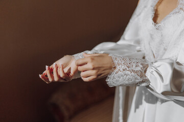 Obraz premium A woman in a white dress is putting on her wedding ring. She is wearing a lace sleeve and has her hands clasped together