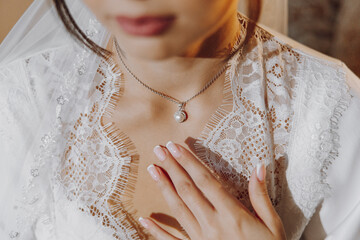 A woman wearing a white lace dress and a pearl necklace. The necklace is a silver chain with a...