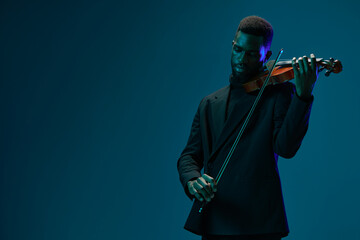Classically elegant musician in black suit playing violin against dark blue background on stage