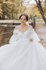 A woman in a white dress is standing in front of a fence. She is wearing a necklace and a veil