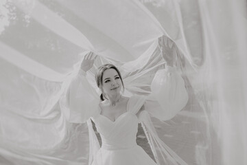 A woman in a white dress is standing in front of a white sheet, with her arms spread out