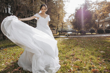 A woman in a white dress is standing in a field of grass with leaves on the ground. She is wearing...