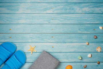 Towel and flip-flops with sea shells and starfish on a blue wooden background. Top view, copy space