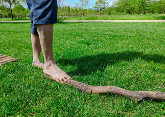 Shot with a close-up on the feet of a Caucasian man walking barefoot: he walks on a branch resting on the grass, it is a stretch of path in nature. Nice sunny day.