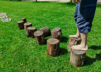 Close-up on the feet of a Caucasian man engaged in a barefoot path: after the path on wooden logs a stretch with stones on a meadow. Nice sunny day.