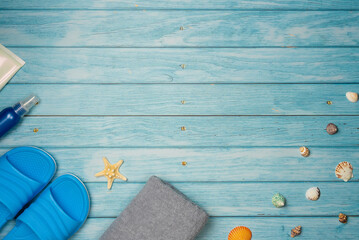 Towel, sunscreen and flip-flops with sea shells and starfish on a blue wooden background. Top view,...