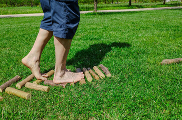 Shot with a close-up on the feet of a Caucasian man walking barefoot: he walks on small trunks arranged horizontally, it is a stretch of path in nature. Nice sunny day.