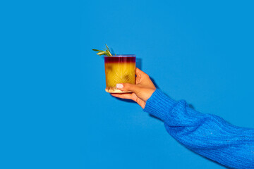 Female hand holding cocktail with orange juice against blue background. New York sour traditional...