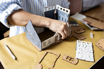 A girl assembles a model of a building from thick cardboard.