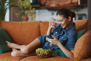 A woman relaxing on sofa with bowl of grapes and using cell phone in cozy home setting