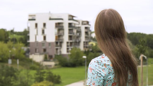 A beautiful young Caucasian woman looks at an apartment complex in a suburban area - rear view
