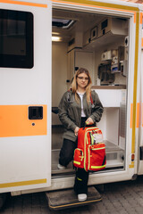 Professional and confident young woman doctor looking on the camera with ambulance background