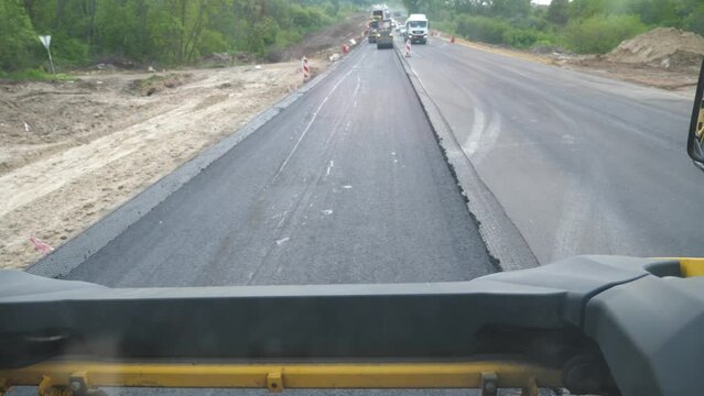 Roller laying new asphalt layer. Special machinery making road. Compactor constructing highway. Roadway repair by heavy machinery. View on process of roadwork from inside cabin of steamroller. Slow mo
