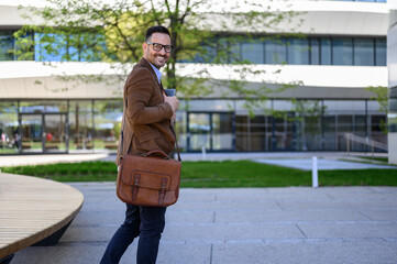 Obraz premium Portrait of happy young businessman with bag looking over shoulder while standing on city street