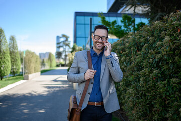 Portrait of happy confident businessman talking over mobile phone while standing by plants on street