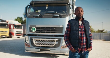 Older African American worker wearing checkered shirt while holding his hands in his pockets. Truck...