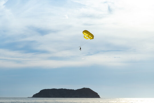 Unrecognizable man in silhouette floating from a parasail wing in the sky, with small island below in the Pacific Ocean, Manuel Antonio, Puntarenas province, Costa Rica