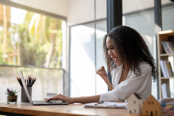 A woman is sitting at a desk with a laptop and a cup of coffee. She is smiling and she is happy