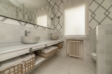 Bathroom with long white marble countertop, with a shower cabin with small gray porcelain tiles,...
