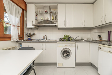 Front image of a kitchen with white furniture with metal handles, gray countertops and wooden...