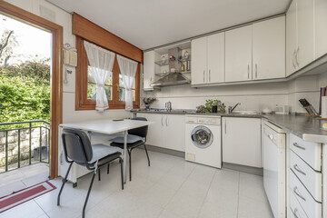 Frontal image of a kitchen with white furniture with metal handles, gray countertops and wooden...