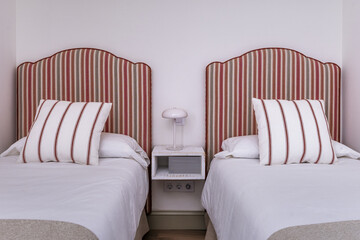Bedroom with twin beds with headboards upholstered in predominantly red striped fabric and a...