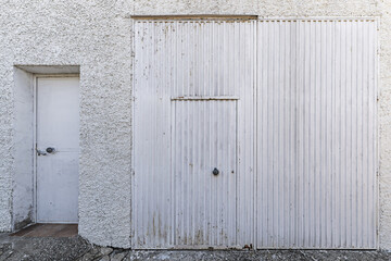 A rough white cement wall with a white metal gate and an accessory door to the other