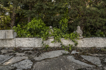 Perimeter fence of a garden with hedges and decorative stone objects and slabs of the same material on the ground