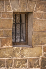 A vintage yellow stone wall with a small window with black bars and wooden frames