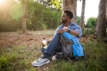 Young hiker drinking energy drink while enjoys resting in nature.