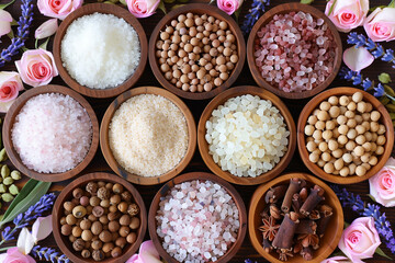 A variety of spices and salt are displayed in wooden bowls. The bowls are arranged in a pattern, with some bowls containing more spices than others