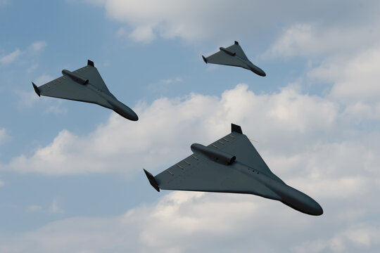 group attack of black drones of modern suicide bombers flying against the background of blue sky and clouds