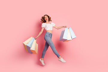 Full length photo of good mood lovely girl wear white top jeans jumping with shopping bags in hands...