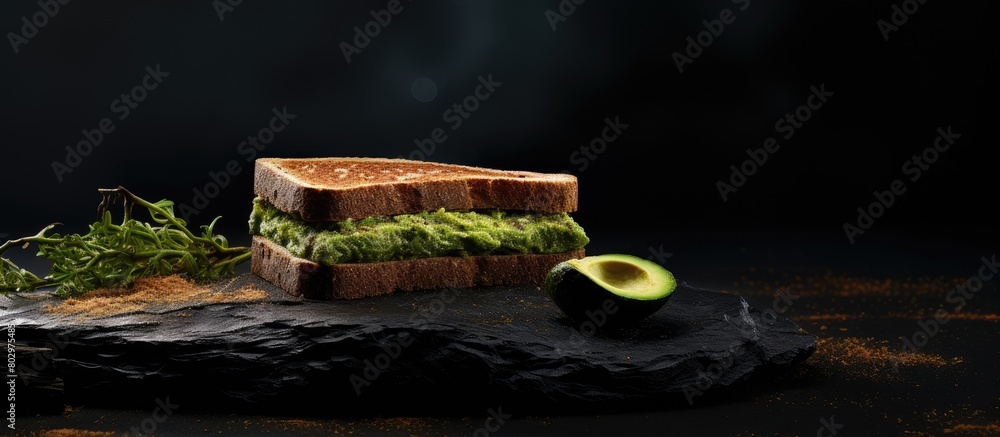 Poster a copy space image depicts toasted bread topped with fresh green avocado on a textured black surface