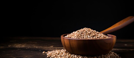 A close up image of buckwheat groats showcased in a wooden bowl alongside a vintage scoop set against a black background Copy space available for adding text