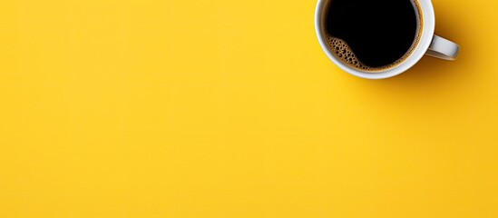 A close up flat lay copy space image showcasing a cup of black coffee on a vibrant yellow background