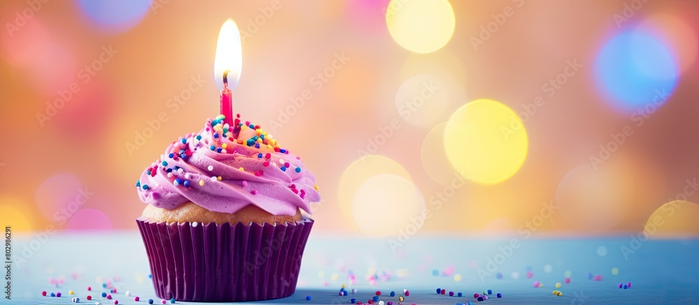 Poster a birthday cupcake with a lit candle and colorful balloons serving as a blurred background providing