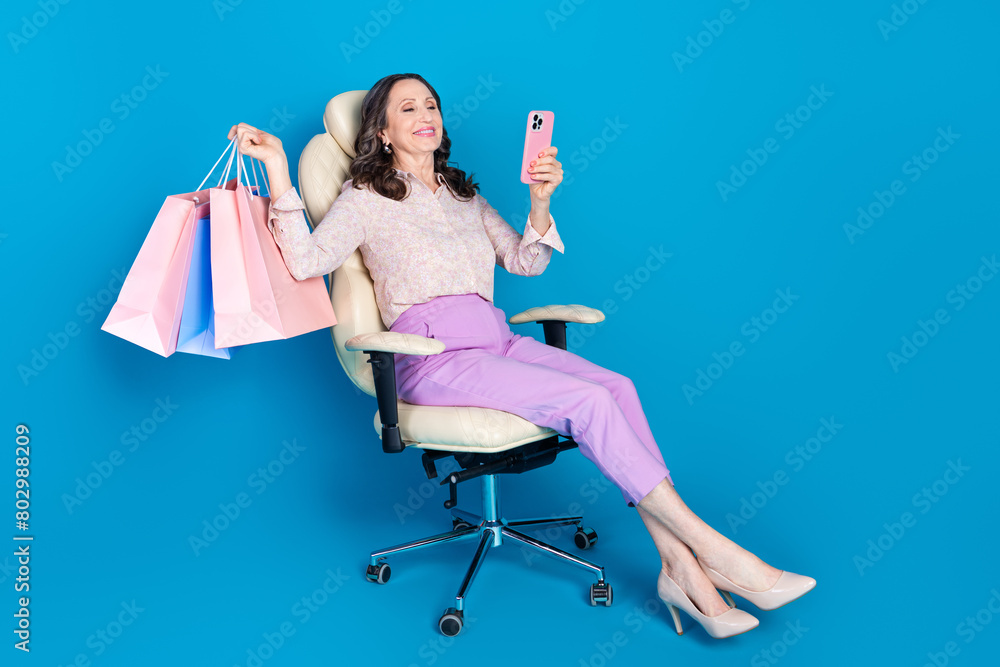 Poster Full length photo of attractive senior woman armchair device shopper dressed stylish formalwear clothes isolated on blue color background