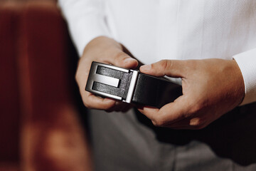A man is holding a belt in his hand. The belt is black and has a silver buckle