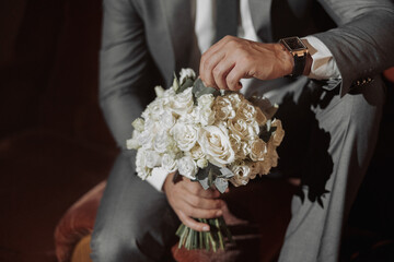 A man in a suit is holding a bouquet of white flowers. The flowers are arranged in a vase and the...