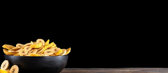 A bowl filled with dried banana slices sits on a black wooden table providing ample space for text in the image - Powered by Adobe