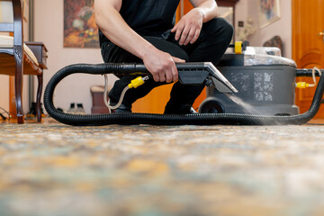 in the apartment a master cleaner waters the carpet with detergent from a professional vacuum...