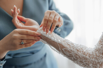 A woman is helping another woman with her wedding dress. The dress is made of lace and has a lot of...